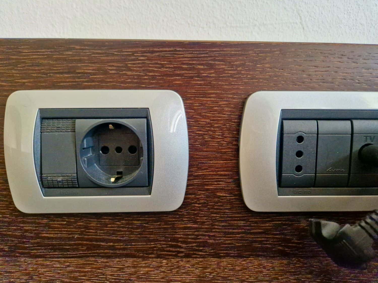 Northern Italy Winter packing list: From Essentials to Specials 10 A close-up of two wall sockets on a wooden surface. The left socket is a European-style power outlet, and the right socket includes connectors for TV and radio. A black power plug is partially inserted into the TV socket.